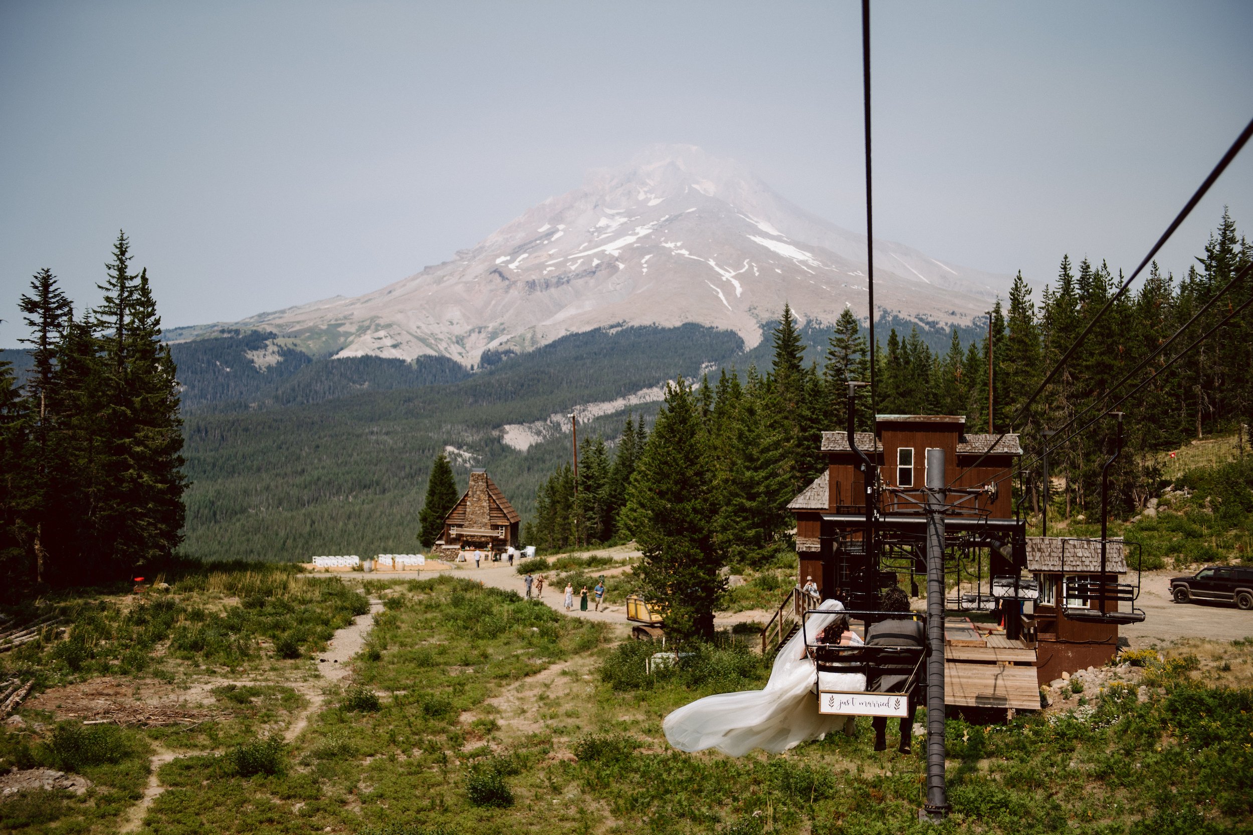 A bride and groom ride a ski lift towards their ceremony site which is located at the bottom of a mountain. Her dress is flowing in the wind as they descend.